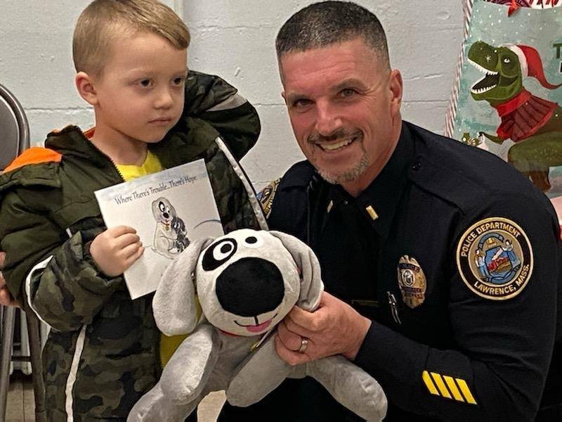A Lawrence, MA police officer giving Trouble the Dog to a child