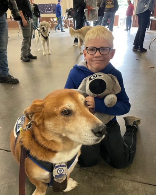 A young boy holding Trouble the Dog next to a therapy dog
